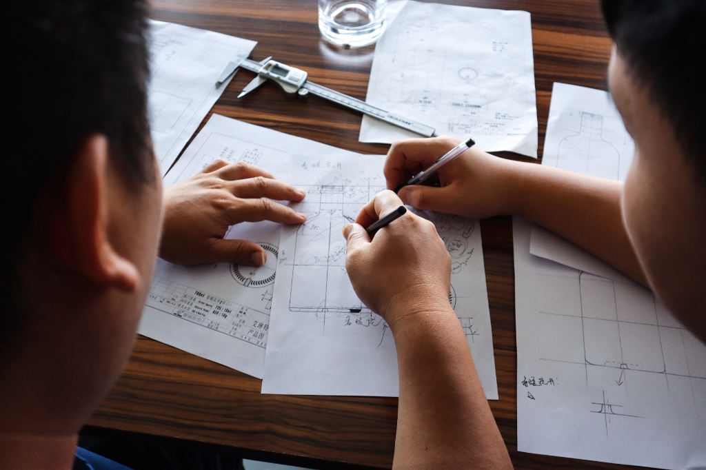 Packaging engineers reviewing technical glass bottle design blueprints and dimensions with calipers